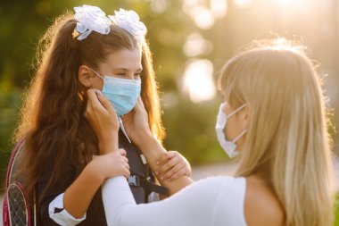 Gün batımında covid-19 sırasında tıbbi maske takan küçük bir kız ve anne. Annesi kızına steril tıbbi maske takıyor. Virüs enfeksiyonundan, salgından ve karantinada salgın hastalıklardan koruyor.. 