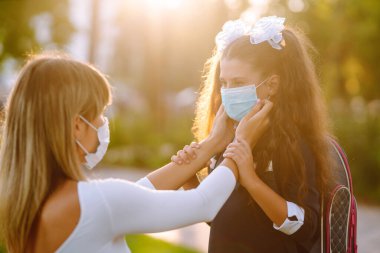 Gün batımında covid-19 sırasında tıbbi maske takan küçük bir kız ve anne. Annesi kızına steril tıbbi maske takıyor. Virüs enfeksiyonundan, salgından ve karantinada salgın hastalıklardan koruyor.. 