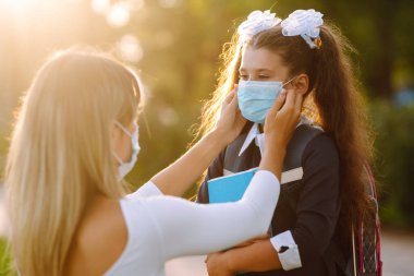 Gün batımında covid-19 sırasında tıbbi maske takan küçük bir kız ve anne. Annesi kızına steril tıbbi maske takıyor. Virüs enfeksiyonundan, salgından ve karantinada salgın hastalıklardan koruyor.. 