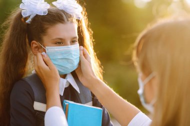 Gün batımında covid-19 sırasında tıbbi maske takan küçük bir kız ve anne. Annesi kızına steril tıbbi maske takıyor. Virüs enfeksiyonundan, salgından ve karantinada salgın hastalıklardan koruyor.. 