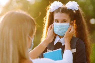 Gün batımında covid-19 sırasında tıbbi maske takan küçük bir kız ve anne. Annesi kızına steril tıbbi maske takıyor. Virüs enfeksiyonundan, salgından ve karantinada salgın hastalıklardan koruyor.. 