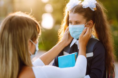 Gün batımında covid-19 sırasında tıbbi maske takan küçük bir kız ve anne. Annesi kızına steril tıbbi maske takıyor. Virüs enfeksiyonundan, salgından ve karantinada salgın hastalıklardan koruyor.. 