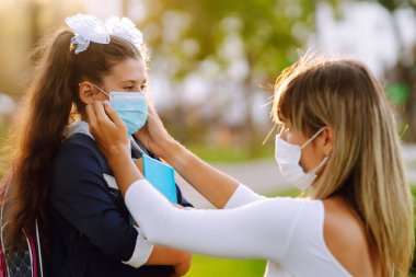 Gün batımında covid-19 sırasında tıbbi maske takan küçük bir kız ve anne. Annesi kızına steril tıbbi maske takıyor. Virüs enfeksiyonundan, salgından ve karantinada salgın hastalıklardan koruyor.. 