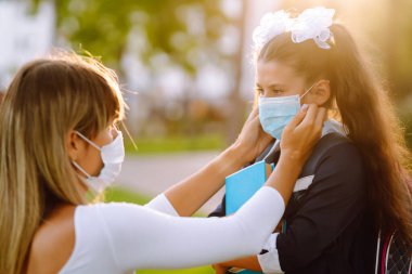 Gün batımında covid-19 sırasında tıbbi maske takan küçük bir kız ve anne. Annesi kızına steril tıbbi maske takıyor. Virüs enfeksiyonundan, salgından ve karantinada salgın hastalıklardan koruyor.. 