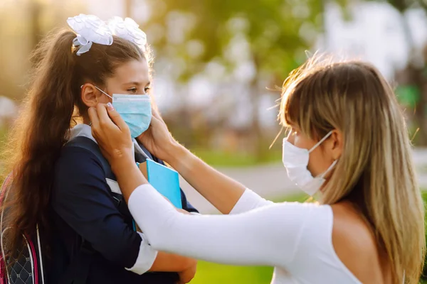 Little girl and mom in medical mask during covid-19 at sunset. Mother puts on his girl sterile medical mask, protect from infection of virus, pandemic, outbreak and epidemic of disease on quarantine.