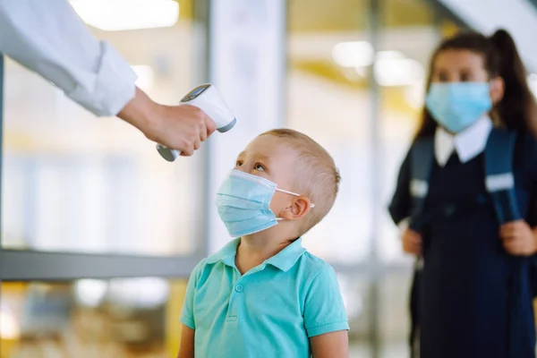 Nurse or doctor checks children body temperature using infrared forehead thermometer (gun) for virus symptom - epidemic outbreak concept. Back to school in quarantine. Covid-19.