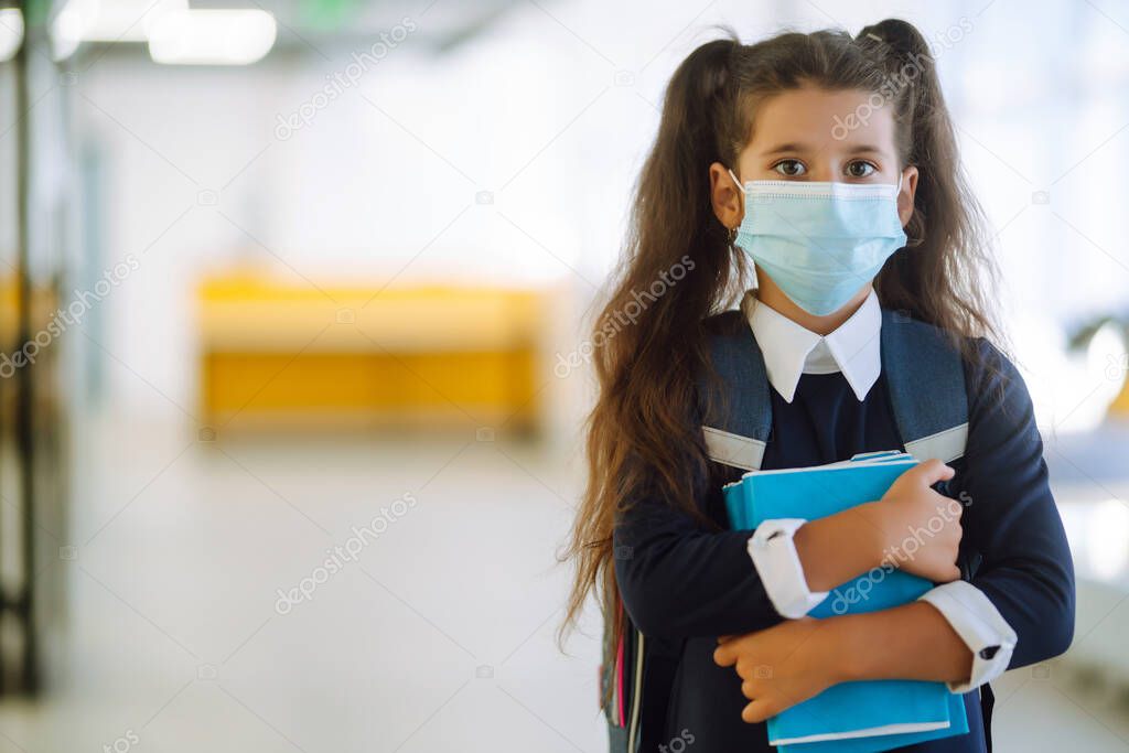 Schoolgirl in a protective mask with a backpack and a textbook in her hands. Security concept, virus protection. Covid-2019.