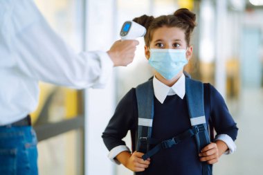 Sıcaklık taraması ve okulda sağlık kontrolü. Tıp maskeli kız öğrenci covid-19 salgınında sınıfta. Okulda termometresi olan öğretmen..