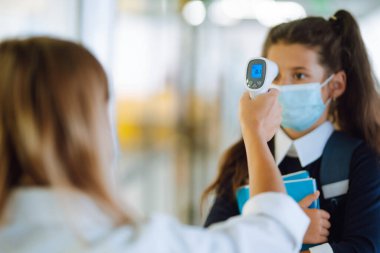 Hemşire ya da doktor, virüs salgını konsepti için kızılötesi alın termometresi (silah) kullanarak vücut ısısını kontrol eder. Karantinaya alınan okula. Covid 19.