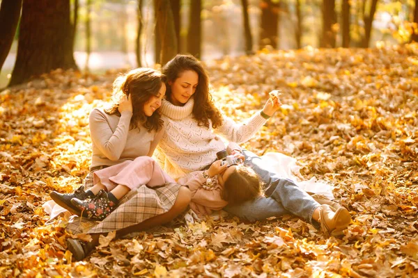 Güz ormanlarında retro kamerayla eğlenen güzel bir çift lezbiyen kadın. Genç homoseksüel aile ve evlatlık genç kızları fotoğraf için poz veriyorlar..