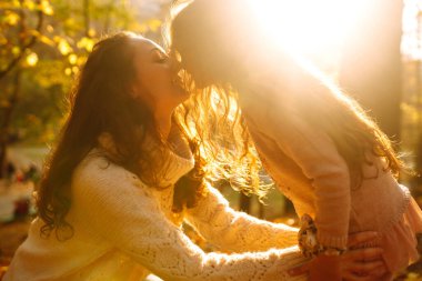 Günbatımında sonbahar ormanlarında yürüyen zarif genç anne ve kız. Anne ve kızı sonbahar parkında kucaklaşıyorlar. Anne ve çocuk sonbaharda birlikte eğleniyorlar. Aile yürüyüşe çıktı.. 