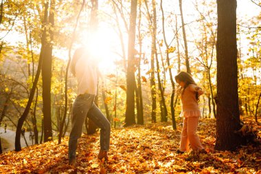 Günbatımında sonbahar ormanlarında yürüyen zarif genç anne ve kız. Anne ve kızı sonbahar parkında kucaklaşıyorlar. Anne ve çocuk sonbaharda birlikte eğleniyorlar. Aile yürüyüşe çıktı.. 