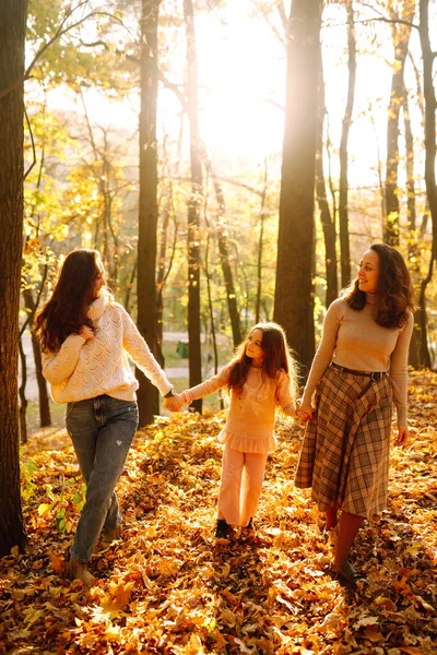 Sonbahar ormanında yürüyen bir çift lezbiyen kadın. Homoseksüel aile kızıyla sonbahar parkında gün batımında oynuyor..