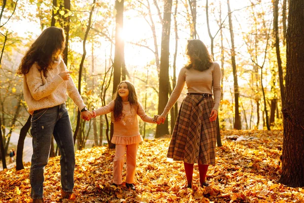 Sonbahar ormanında yürüyen bir çift lezbiyen kadın. Homoseksüel aile kızıyla sonbahar parkında gün batımında oynuyor..