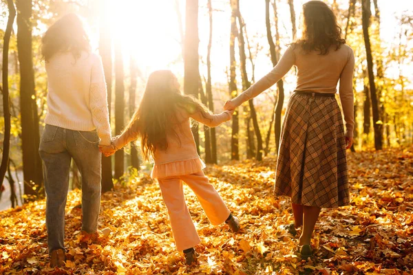 Sonbahar ormanında yürüyen bir çift lezbiyen kadın. Homoseksüel aile kızıyla sonbahar parkında gün batımında oynuyor..