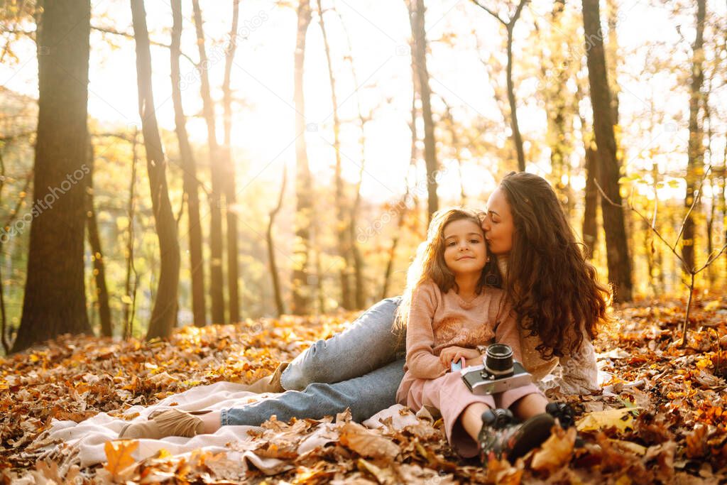Stylish young Mother and daughter walking in the autumn forest at sunset. Mother and daughter embrace in autumn park. Mom and child having fun together in autumn. Family on a walk. 