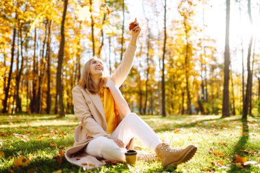 Mutlu genç kadın sonbahar parkında eğleniyor ve sarı yapraklarla oynuyor. Sonbahar moda konsepti.