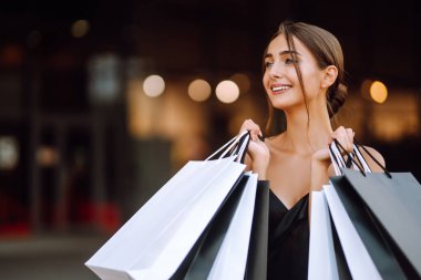 Moda kadını alışverişi seviyor. Zarif bir kadın elinde siyah beyaz alışveriş çantaları olan siyah bir elbise giyer. Kara Cuma, satış, tüketim, yaşam tarzı konsepti.