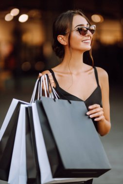 Moda kadını alışverişi seviyor. Zarif bir kadın elinde siyah beyaz alışveriş çantaları olan siyah bir elbise giyer. Kara Cuma, satış, tüketim, yaşam tarzı konsepti.