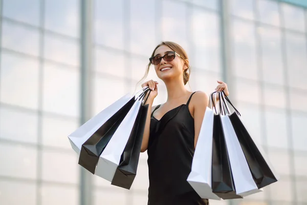 買い物中の女性 買い物の後に街を歩くショッピングバッグと黒のドレスのファッション女性 黒の金曜日 消費者 ライフスタイルの概念 — ストック写真