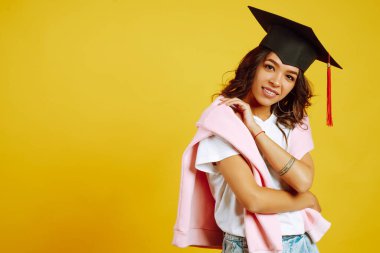Mezuniyet şapkası takmış mezun bir kadının portresi. Eğitim, eğitim, üniversite, üniversite, mezuniyet konsepti sarı pankart üzerine.
