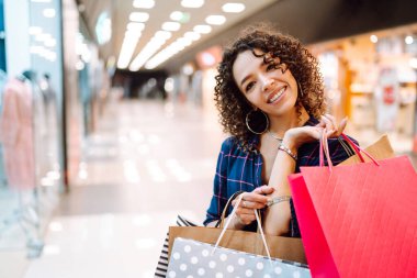 Alışveriş merkezinde alışveriş yapan gülümseyen bir kadın. Alışveriş sonrası paketleri olan genç bir kadın. Satın almalar, Kara Cuma, indirimler, satış konsepti.