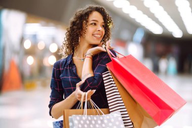 Alışveriş merkezinde alışveriş yapan gülümseyen bir kadın. Alışveriş sonrası paketleri olan genç bir kadın. Satın almalar, Kara Cuma, indirimler, satış konsepti.