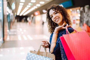 Alışveriş merkezinde alışveriş yapan gülümseyen bir kadın. Alışveriş sonrası paketleri olan genç bir kadın. Satın almalar, Kara Cuma, indirimler, satış konsepti.