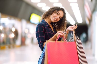 Alışveriş merkezinde alışveriş yapan gülümseyen bir kadın. Alışveriş sonrası paketleri olan genç bir kadın. Satın almalar, Kara Cuma, indirimler, satış konsepti.