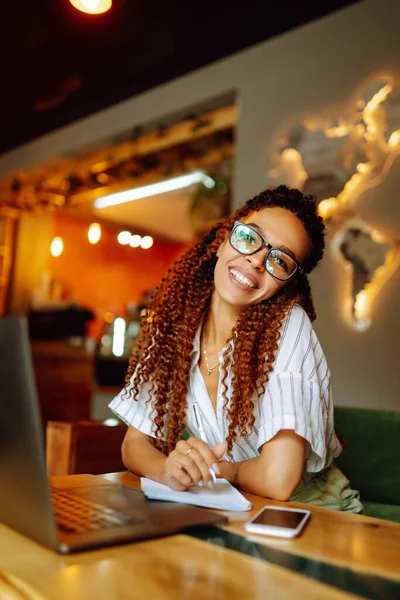 Young freelancer woman using laptop computer sitting at cafe table. Smiling woman working online or studying and learning while using notebook. Business People Concept