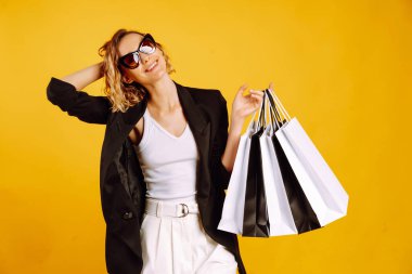 Alışveriş torbalarıyla güzel bir kadının portresi. Sarı arka planda duran siyah beyaz çantalı genç bir kadın. Satın almalar, Kara Cuma, indirimler, satış konsepti.