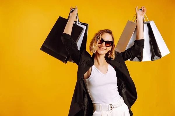 Portrait of nice charming woman with shopping bags. Young woman with black and white bags posing on yellow background. Purchases, black friday, discounts, sale concept.