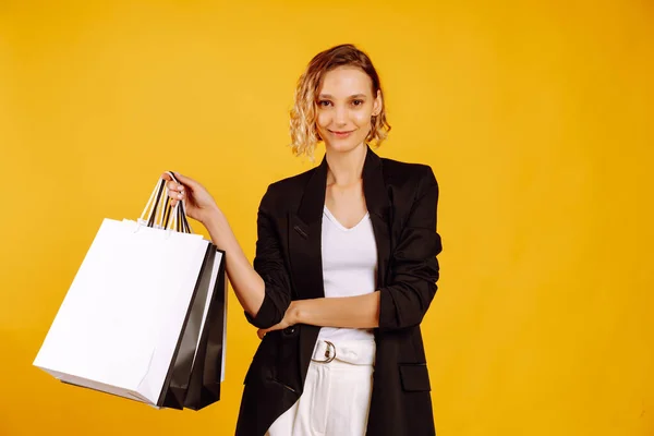 一个带购物袋的漂亮迷人女人的画像 一个年轻的女人 背着黑色和白色的包在黄色的背景上摆着姿势 黑色星期五 销售概念 — 图库照片