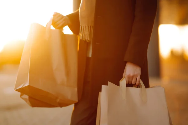 Shopping bags in the hands at sunset. Hand of young man with paper bags with purchases. Consumerism, purchases, shopping, black friday, lifestyle concept.