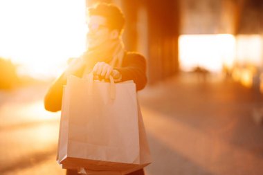 Elinde alışveriş torbaları olan genç bir adamın eli. Yakışıklı adam alışveriş torbalarını tutuyor. Tüketim, alım satım, alışveriş, kara cuma, yaşam tarzı konsepti.