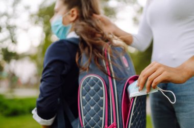 Annem COVID-19 karantinası sırasında okula dönerken bir kızın sırt çantasına koruyucu bir steril maske takıyor..
