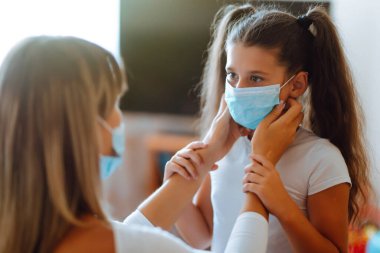 Annem, kızına evde steril tıbbi maske takıyor. Bir anne ve kız, bulaşıcı hastalıklara ve gribe karşı koruyucu bir maske kullanıyor. COVID-19 karantina.
