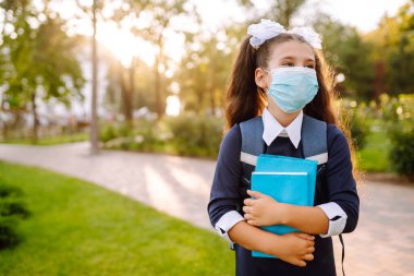COVID-19 karantinası sırasında okula dönerken koruyucu steril maskeli okul kızı. 