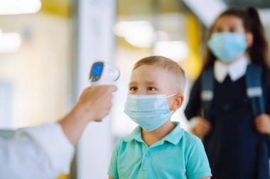 Okuldaki çocukta sıcaklık kontrolü. Hemşire ya da doktor çocukların vücut ısılarını virüs belirtileri için kızılötesi alın termometresi (silah) kullanarak kontrol eder. Covid 19.