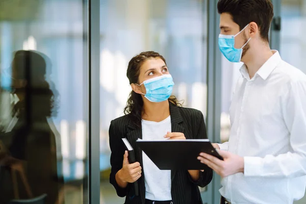 医療面のマスクを身に着けているビジネスの同僚はオフィスで一緒に仕事の問題を議論する 隔離都市でのパンデミック時のチームワーク Covid — ストック写真