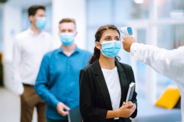 Hastalık kontrol uzmanları ofise girmeden önce alnındaki sıcaklığı kontrol etmek için kızılötesi termometre cihazı kullanırlar. Ofis çalışanlarının ateşini düşürmek. Covid 19.