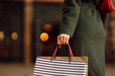 Alışveriş torbaları ellerde. Sokakta yürürken hediye aldıktan sonra çok renkli çantaları olan şık bir kadının eli. Tüketim, alım, satış, Kara Cuma konsepti.