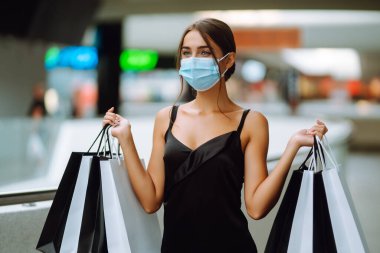 Alışveriş merkezinde alışveriş torbaları taşıyan koruyucu tıbbi maskeli şık bir kadın. Coronavirus Covid-19 salgını sırasında alışveriş. Satın almalar, Kara Cuma, indirimler, satış konsepti. 