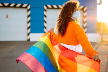 LGBT gökkuşağı bayrağı ve koruyucu maskeli genç kadın salgının yayılmasını önlüyor ve koronavirüs ve salgın COVID-19 'u tedavi ediyor..