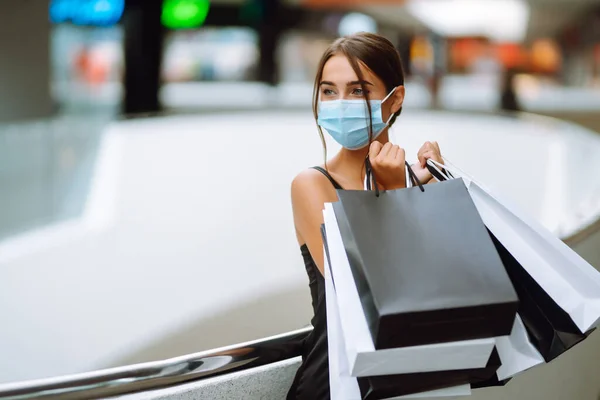 ショッピングバッグをモール内を歩くと保護医療用マスクでファッショナブルな女性 コロナウイルスCovid 19パンデミックの間の買い物 黒の金曜日 販売の概念 — ストック写真