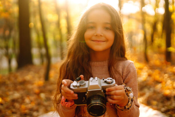 Portrait of little pretty girl  having fun in the autumn forest with retro camera. Happy girl with long brown hair in the autumn park