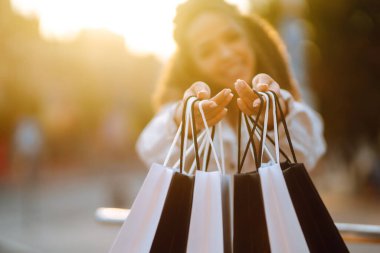 Bir kadının elini yakın tut ve siyah beyaz alışveriş torbalarını tut. Gün batımında alışveriş yaptıktan sonra paketleri olan genç bir kadın. Satın almalar, Kara Cuma, indirimler, satış konsepti.