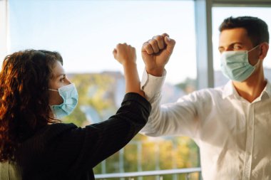 Coronavirus 'un (COVID-19) yayılmasını önlemek için dirsek seği selamı. Ofiste birbirini selamlarken dirseklerini birbirine çarpan yüz maskesi takan iki meslektaş.. 