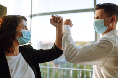 Coronavirus 'un (COVID-19) yayılmasını önlemek için dirsek seği selamı. Ofiste birbirini selamlarken dirseklerini birbirine çarpan yüz maskesi takan iki meslektaş.. 