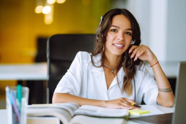 Kulaklık takan genç bir kadın dizüstü bilgisayar kullanarak webinar izliyor ya da web kamerasıyla görüntülü konuşma yapıyor. E-öğrenim eğitim konsepti. İnternette çalış.